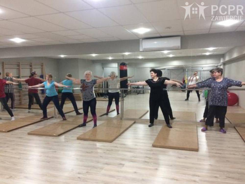 Zdjęcie: Grupa kobiet wykonuje ćwiczenia w sali gimnastycznej tyłem do lustra